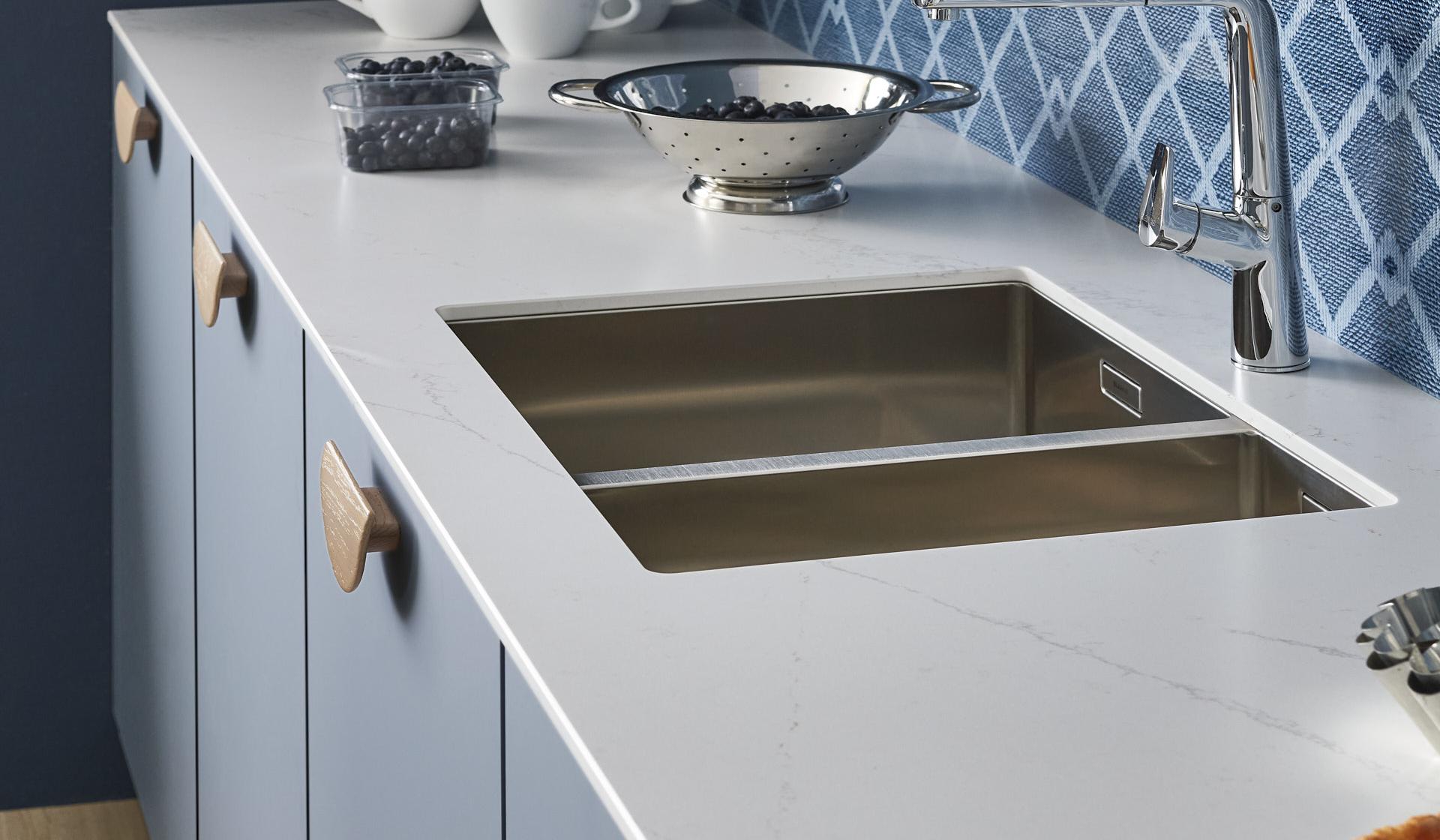 Küchenzeile mit Marmor-Arbeitsplatte pastellgraublaue Fronten Holzgriffe blau gemusterter Spritzschutz niedrig